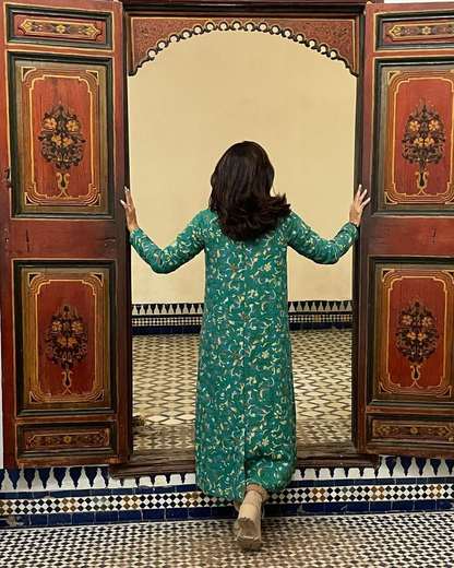 Viajera abriendo unas puertas de madera pintada hacia un patio con azulejos en Marrakech